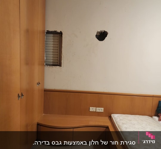 חדר שינה עם חור בקיר מעל גב המיטה לפני תיקון